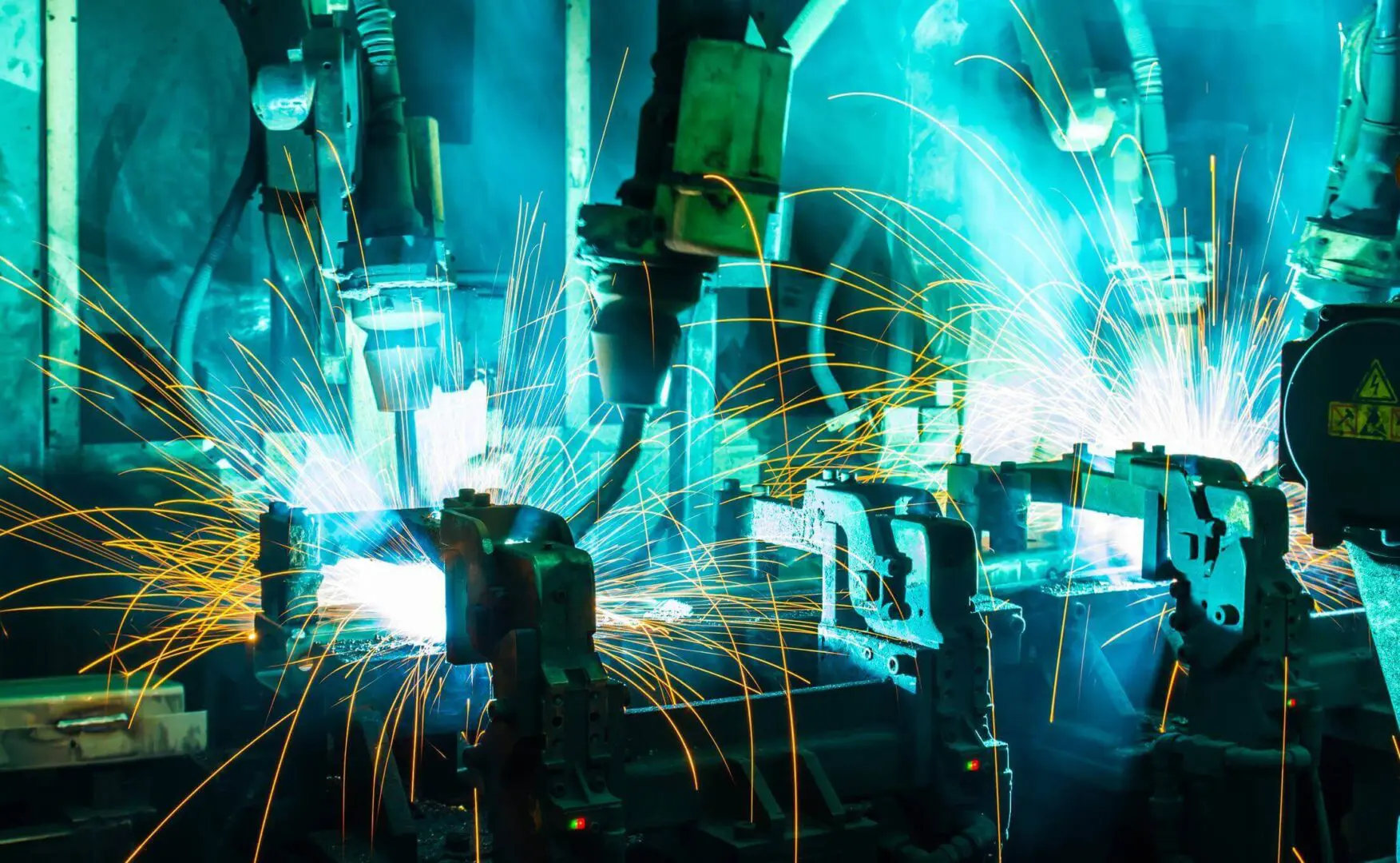 Robotic arms in a factory are welding metal, with bright sparks flying around.