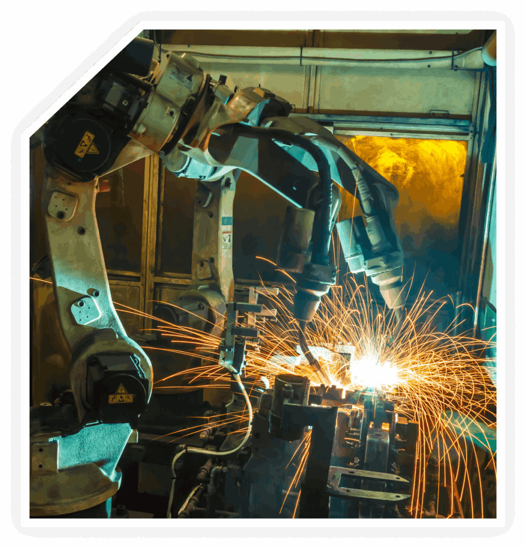 Industrial robotic arms performing welding tasks with bright sparks flying in a factory setting.