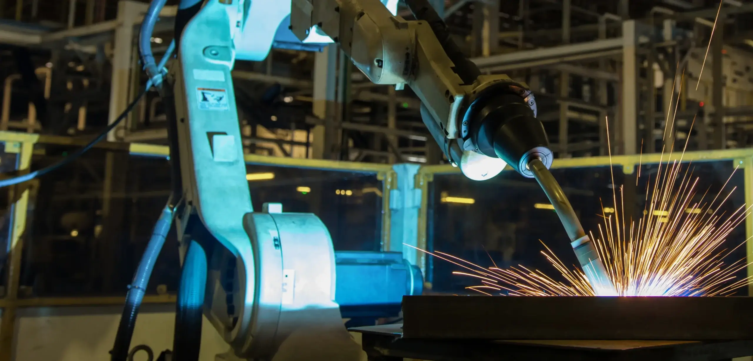 A robotic arm performs welding in a factory, emitting bright sparks.
